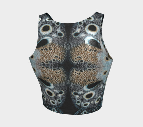 A women's sleeveless racerback crop top with a body-hugging fit. The top features a detailed, kaleidoscopic all-over print inspired by deer pelt. The symmetrical, Rorschach-like design includes abstract spots and textures in shades of brown, blue, black, and grey, creating an intricate pattern that resembles a deer pelt.